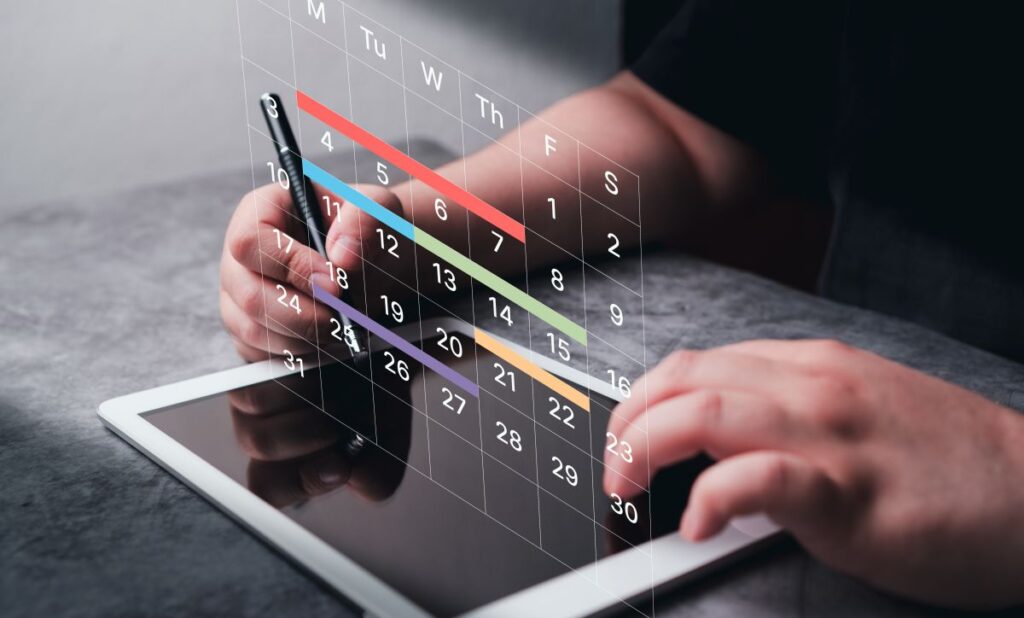 This image shows a person using a stylus on a tablet with a digital calendar interface projected above the screen. The calendar includes dates and color-coded horizontal bars, suggesting task planning, scheduling, or project tracking in a digital workspace.